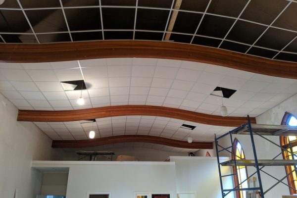 A church under construction with workers installing wooden beams for the ceiling.