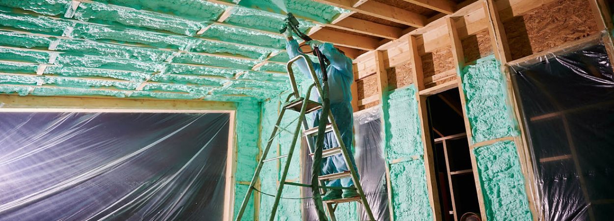 A man standing on a ladder in a room with insulation.