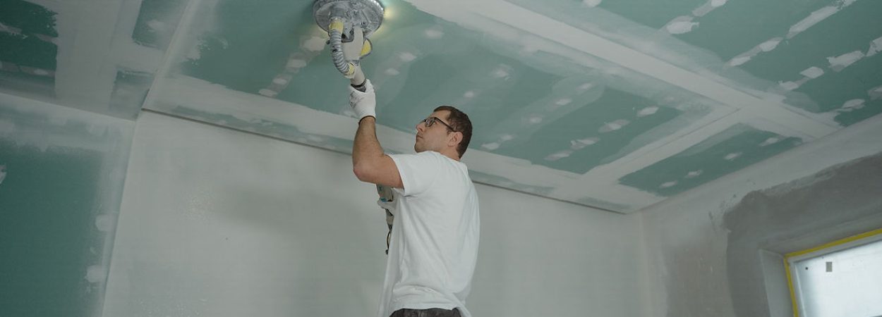A man in a white shirt painting a ceiling with a roller brush.